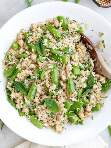 Snap pea, quinoa, and chickpea salad in a bowl with a wooden spoon.