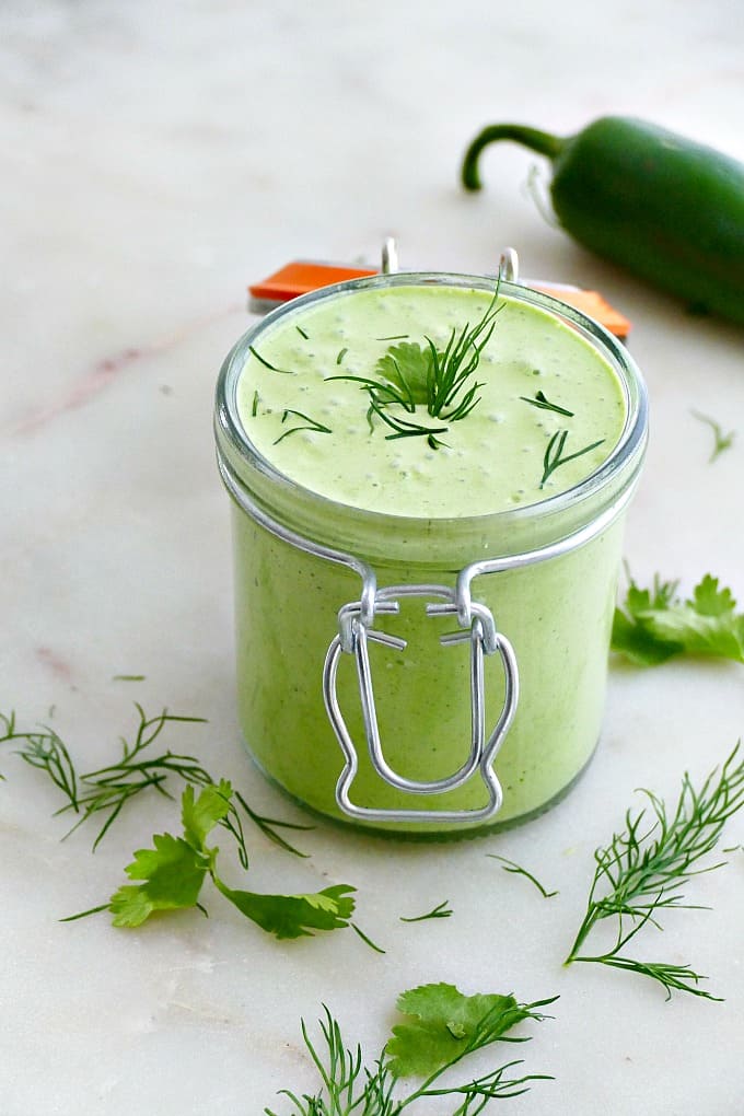 green jalapeno sauce with herbs on top in a container on a counter