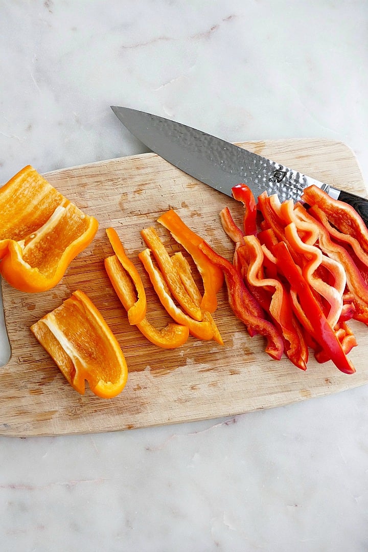thinly sliced red and orange bell peppers on a cutting board with a chef's knife