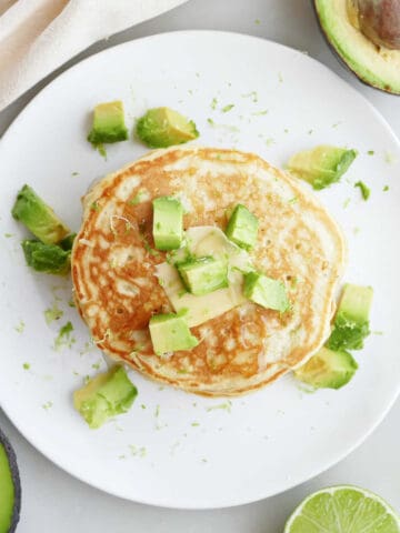Avocado pancakes on a plate next to sliced avocadoes.